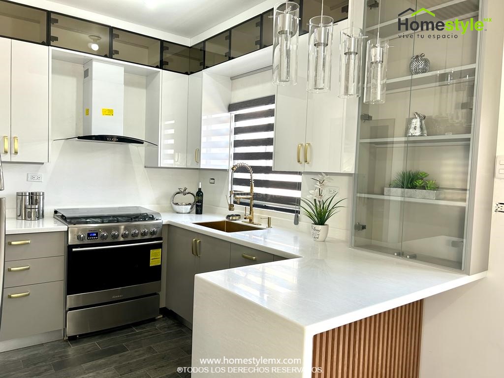 Cocina en forma de J con barra comedor. Diseñada en Melamina Gris para gabinetes inferiores y MDF Alto Brillo Luxe Blanco para gabinetería superior, Vidrio en puertas superiores y detalles en lambrin cedro bajo la barra. Con una cubierta de Superficie Solida Wilsonart Artic Dune.