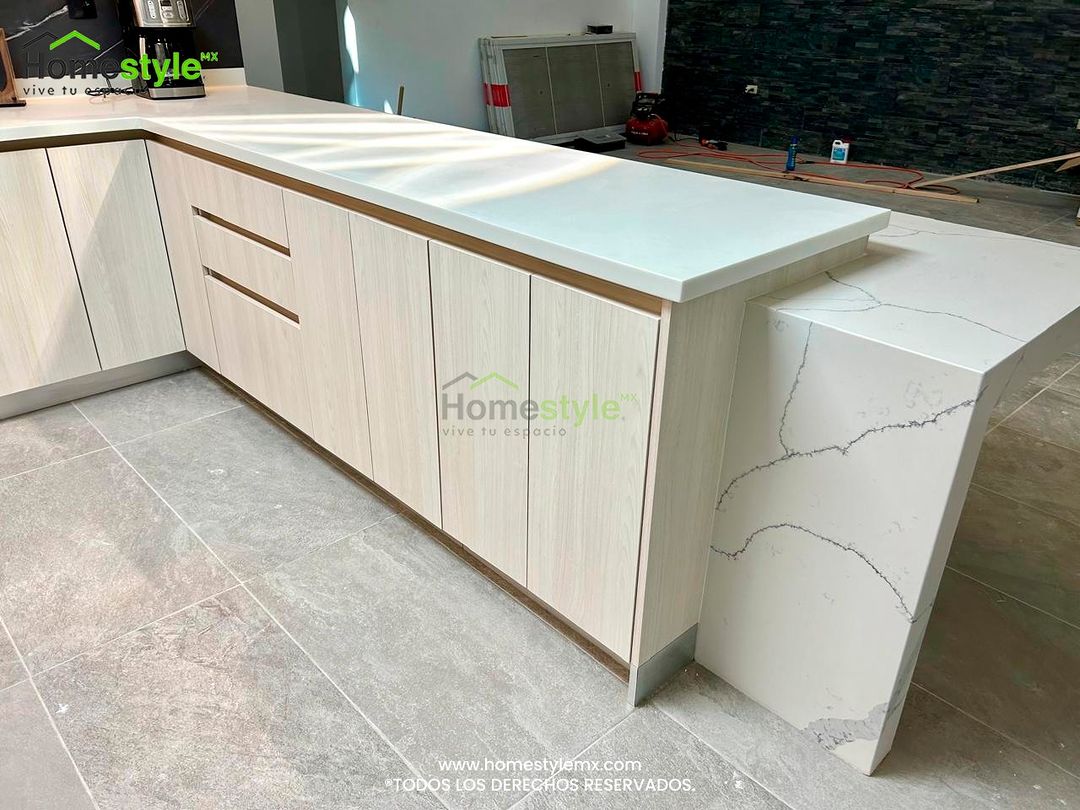 Cocina en L con barra diseñada en Melamina Teka Ártico para gabinetes inferiores y MDF Alto Brillo Blanco para gabinetes superiores. Backsplash en Melamina Vizcaya. Cubierta de Superficie Sólida Frosty White y en la sobre barra cubierta de Cuarzo Carrara. Instalación y venta de iluminación tiras LED.