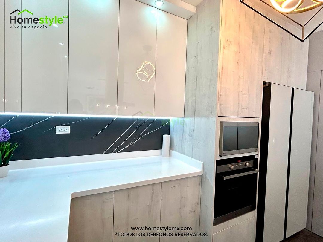 Cocina en forma de J con barra diseñada en Melamina Alaska para la gabinetería inferior, MDF Alto Brillo Blanco en gabinetes superiores, Melamina Vizcaya para Backsplash. Cubierta Superficie Sólida Frosty White en cocina y Black Onyx Mirage en sobre barra, puertas estilo acordeón en cuarto de lavado en Melamina Gris Humo. Se le agrego Iluminación LED luz fría y spots.